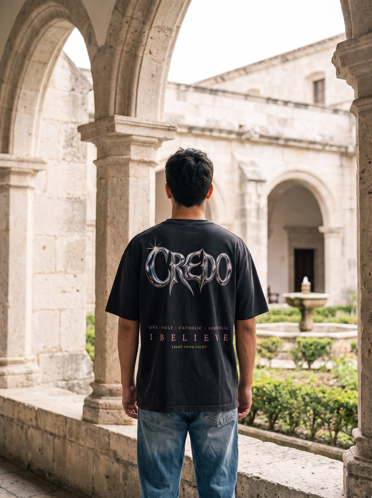Credo — Nicene Tee, back, black. In a monastery cloister.